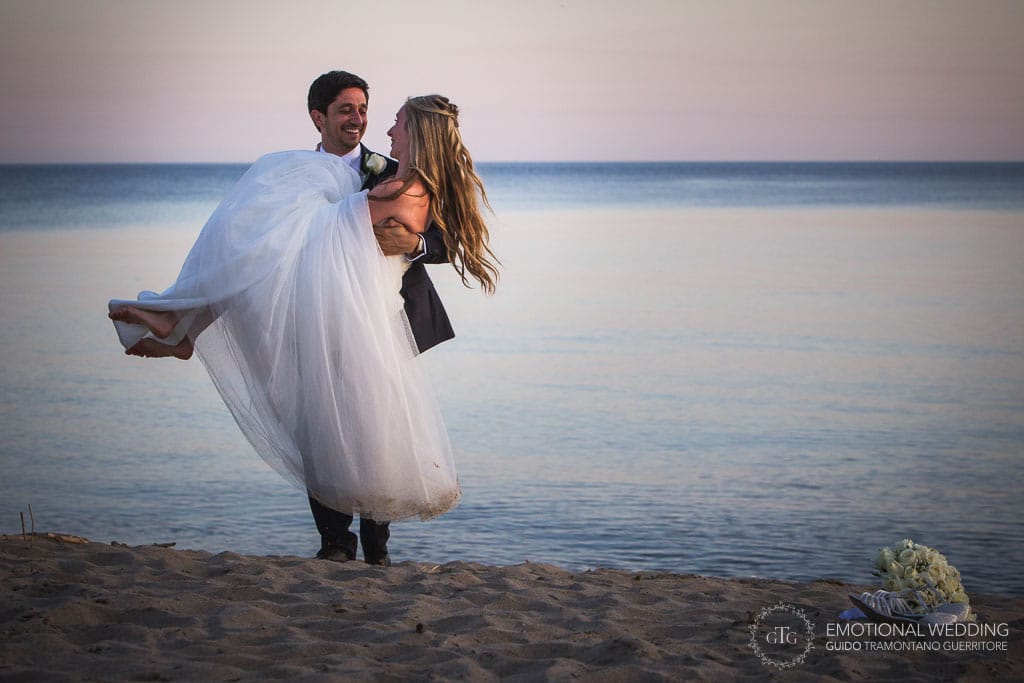 sposo prende in braccio la sposa su una spiaggia a un matrimonio nel Cilento