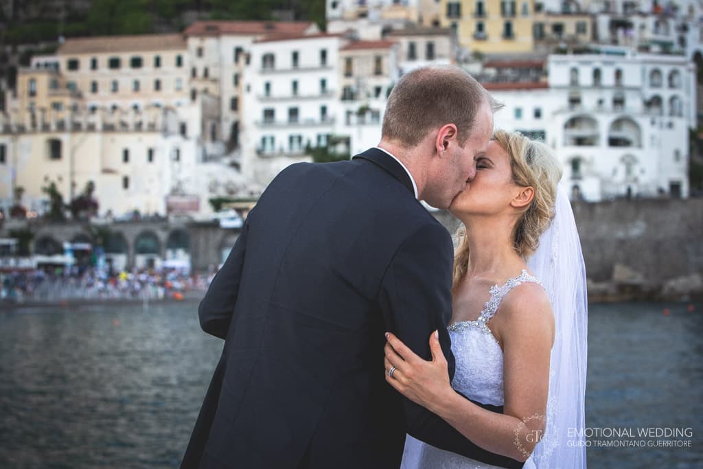 wedding couple kissing on the pier and town in the background in amalfi coast