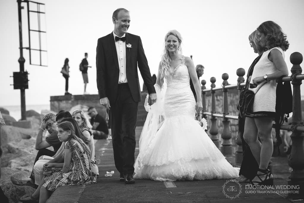 bride and groom walk among people on the pier in Amalfi Coast