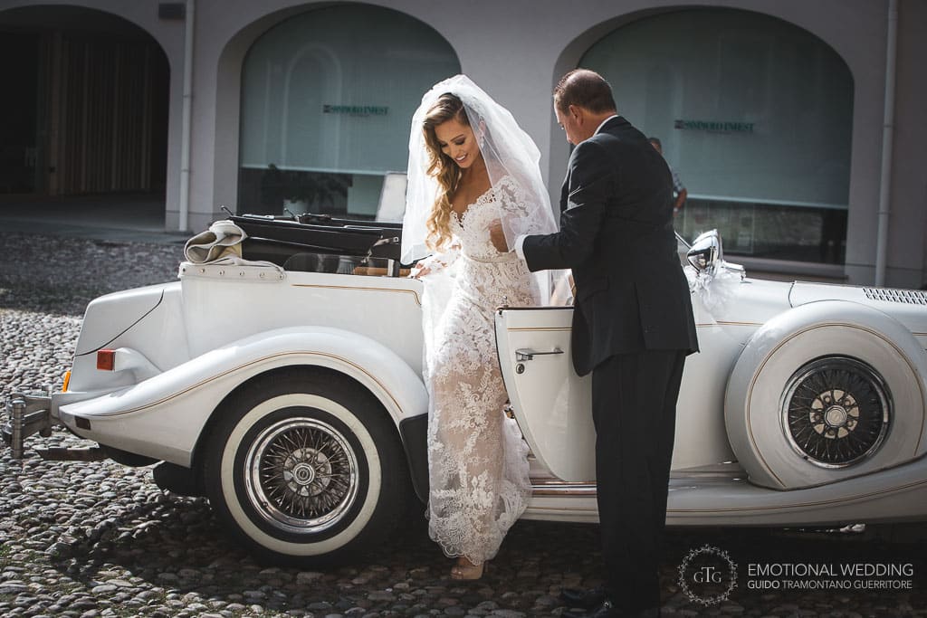 a bride gets out of a vintage car in from of the church