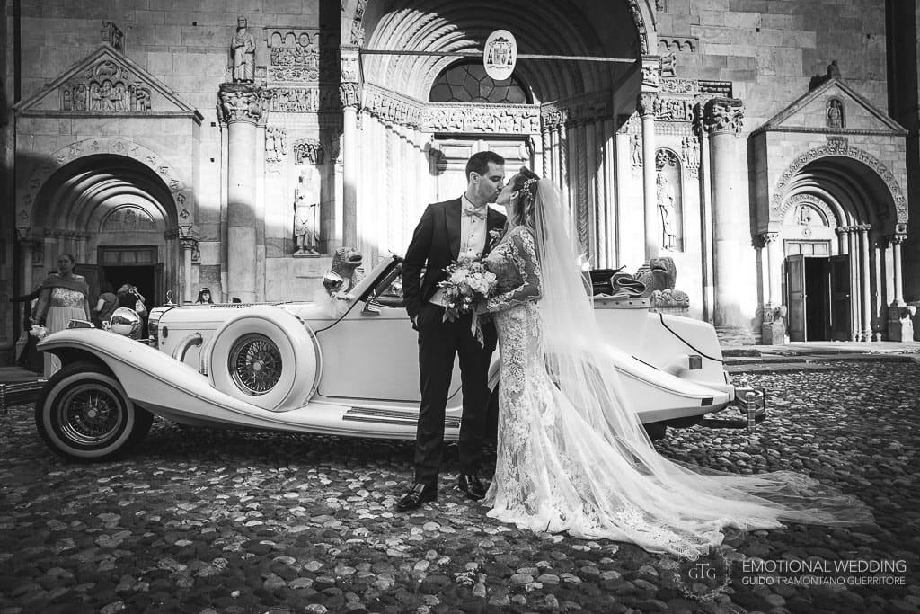 bride and groom kissing by their vintage car in front of the fidenza cathedral