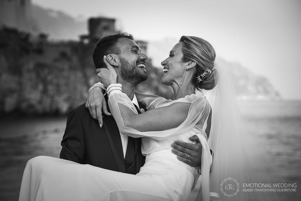 groom takes the bride into his arms on the pier in Amalfi