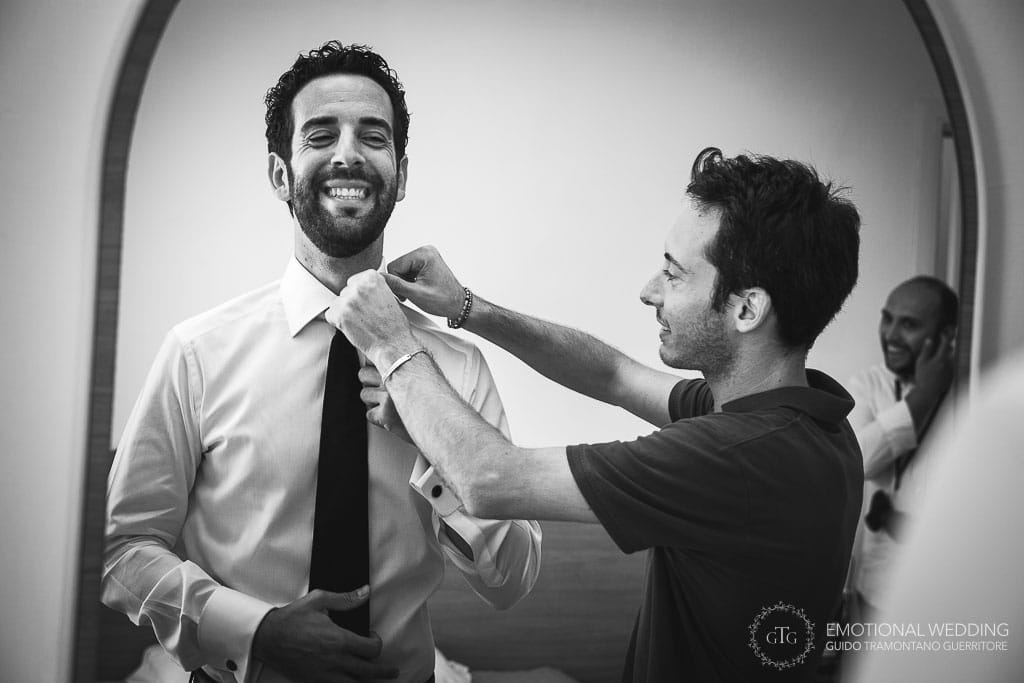 a groom's friend helps wearing the tie
