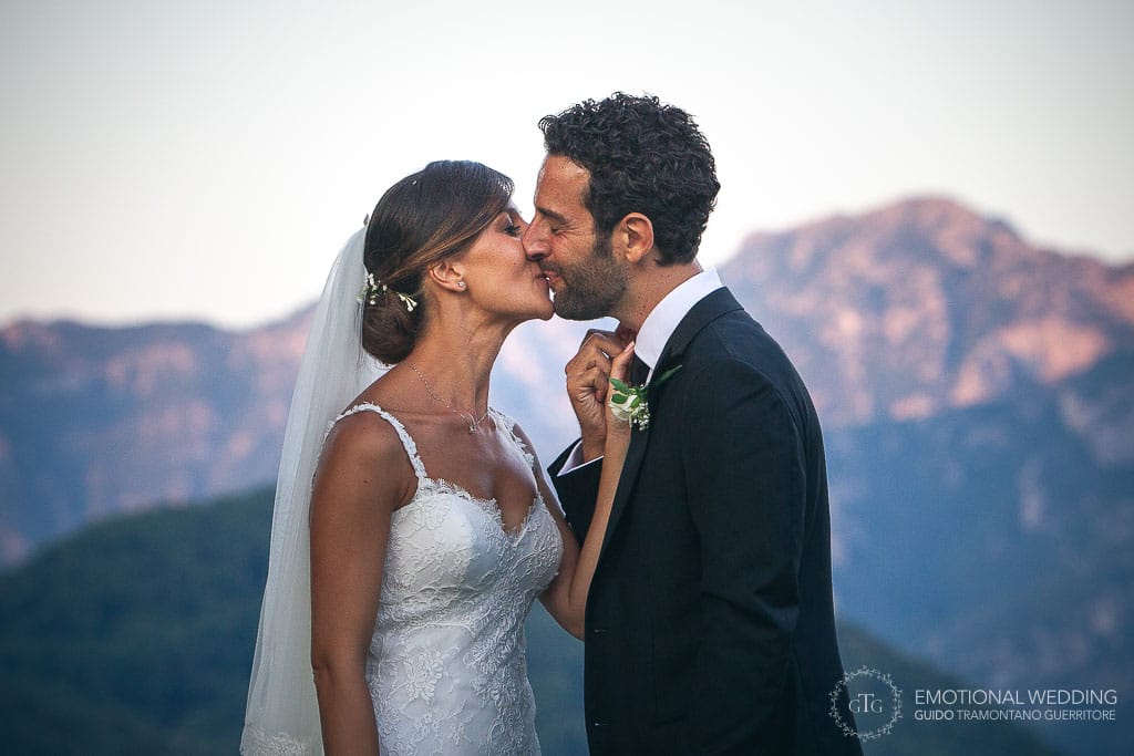 bride and groom kissing in a garden in ravello and mountains at sunset in the background