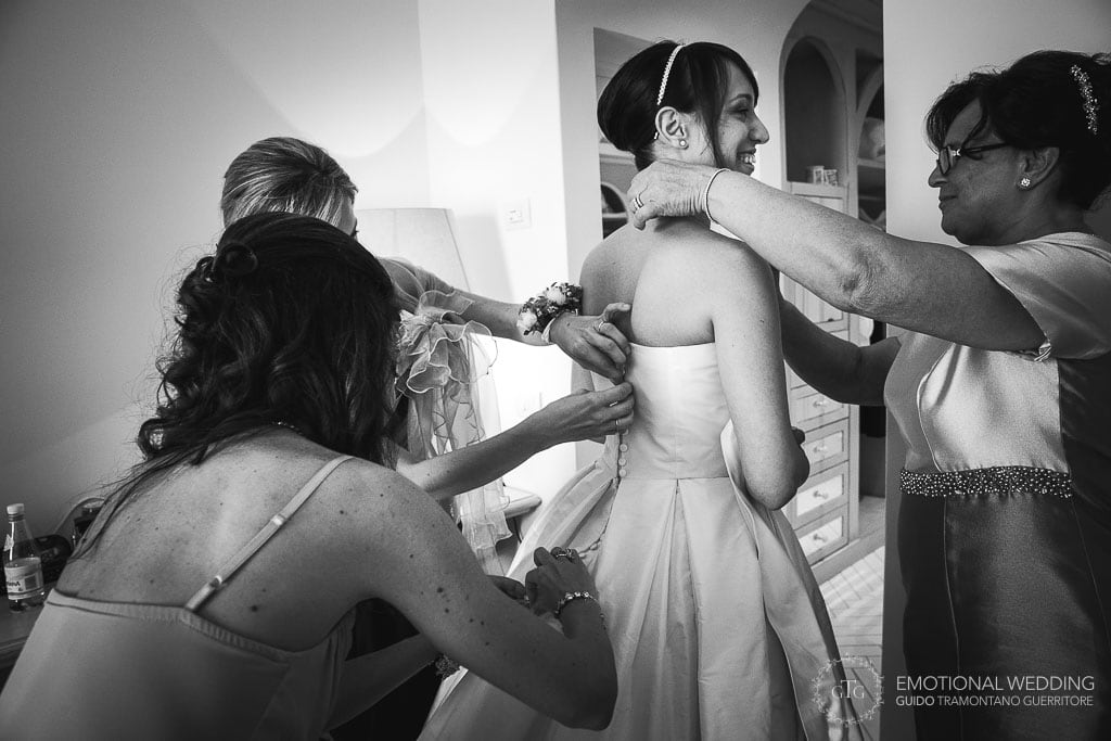bridesmaids and mother of the bride buttoning up the bride's dress at hotel room in praiano