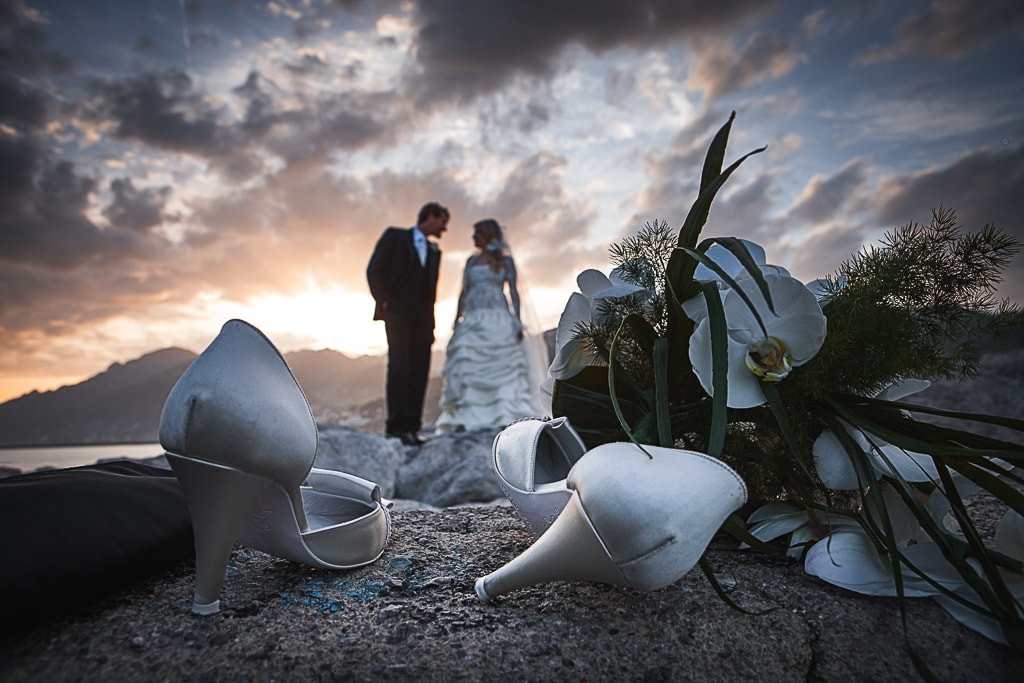 wedding shoes in the foreground and a wedding couple at sunset in the background on the amalfi coast