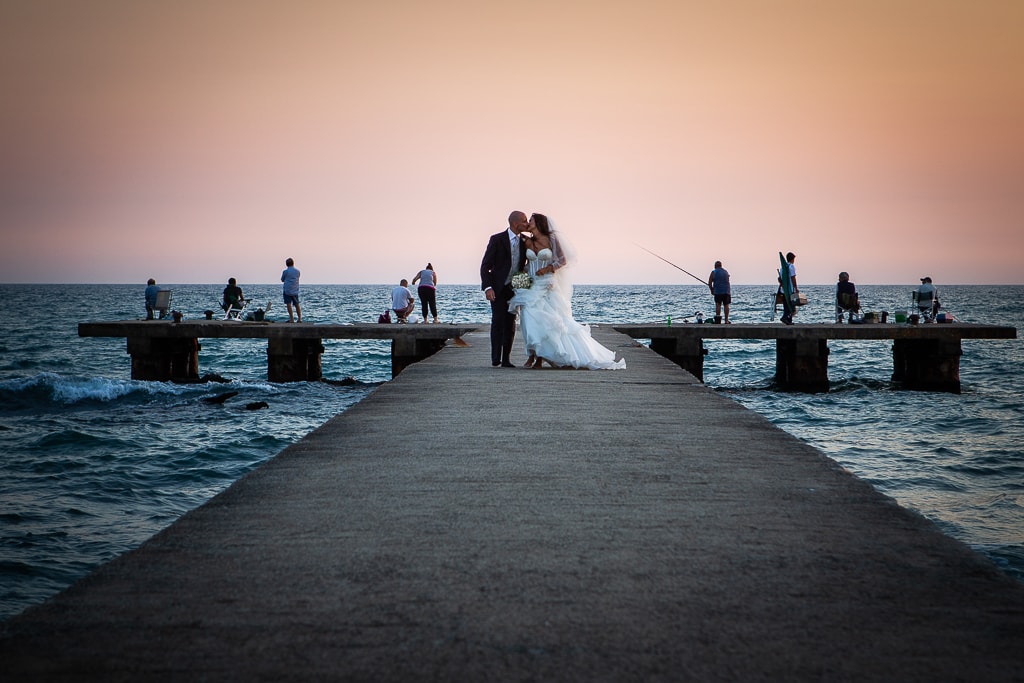 wedding couple on a pier and fishermen in the background