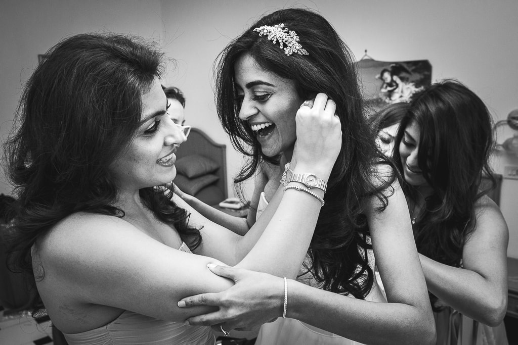 hindu bride laughs while the bridesmaids helps her getting ready