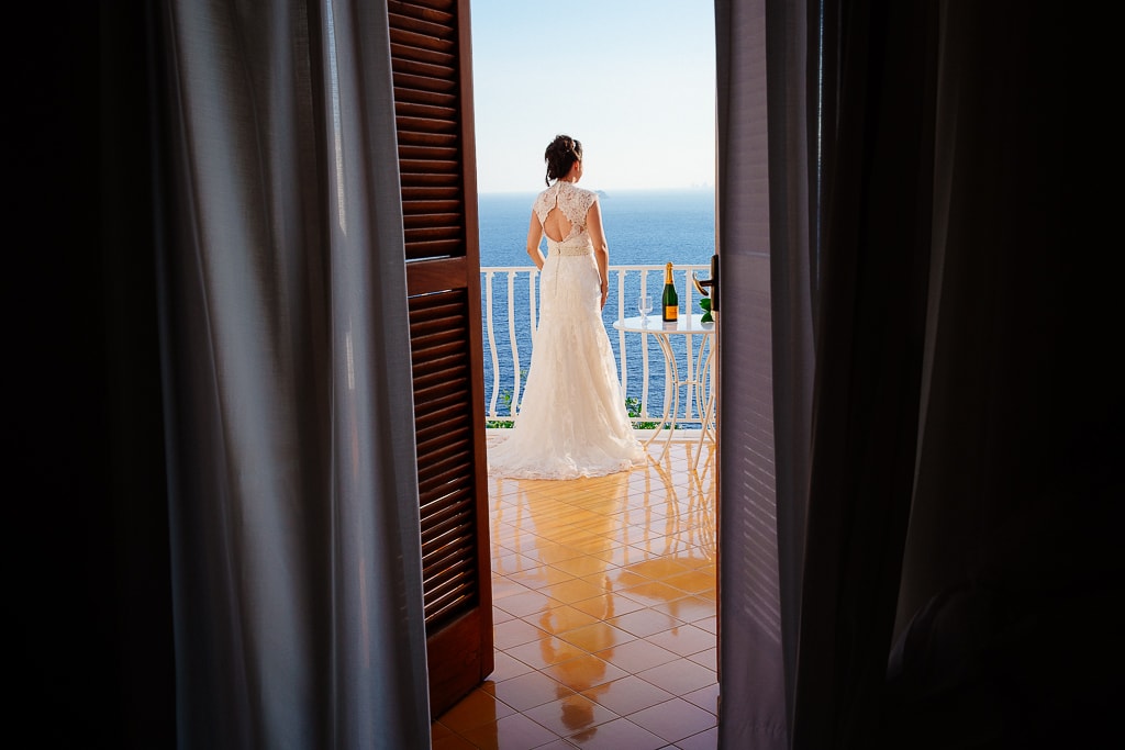 bride enjoys the view from a balcony of her hotel room in amalfi coast
