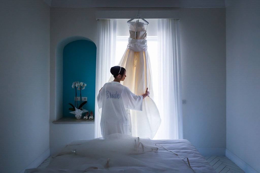 a bride admires her wedding dress hanging on the window at hotel tramonto d'oro on the amalfi coast