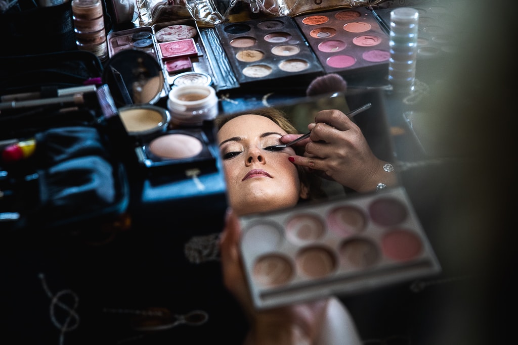 bride wearing make-up seen in a little mirror surrounded by make-up