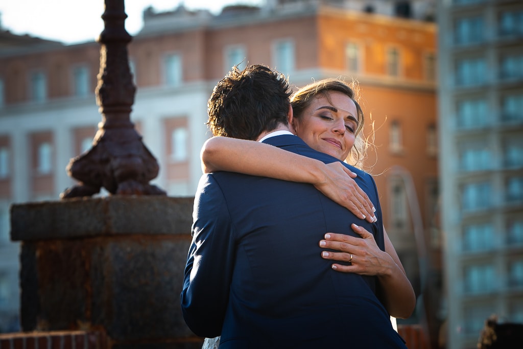 a wedding couple hug with and city of naples in the background at sunset