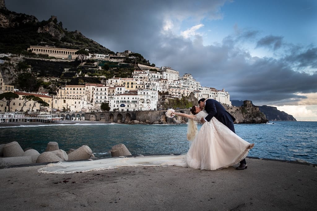 wedding couple kissing on the pier in amalfi with the town of atrani in the background