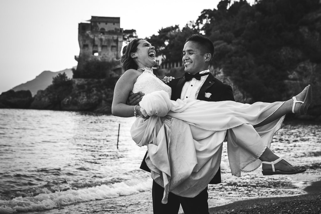 groom holding the bride in his arms and laughing on a beach in amalfi coast