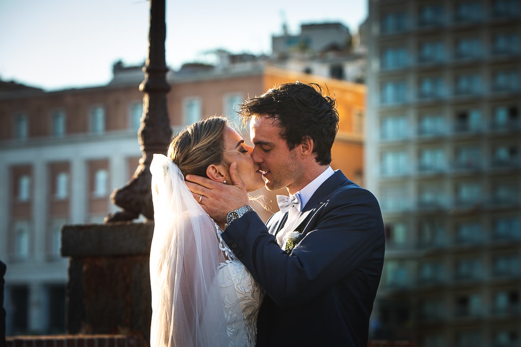 a very romantic kiss of a wedding couple with the city of naples in the background at sunset