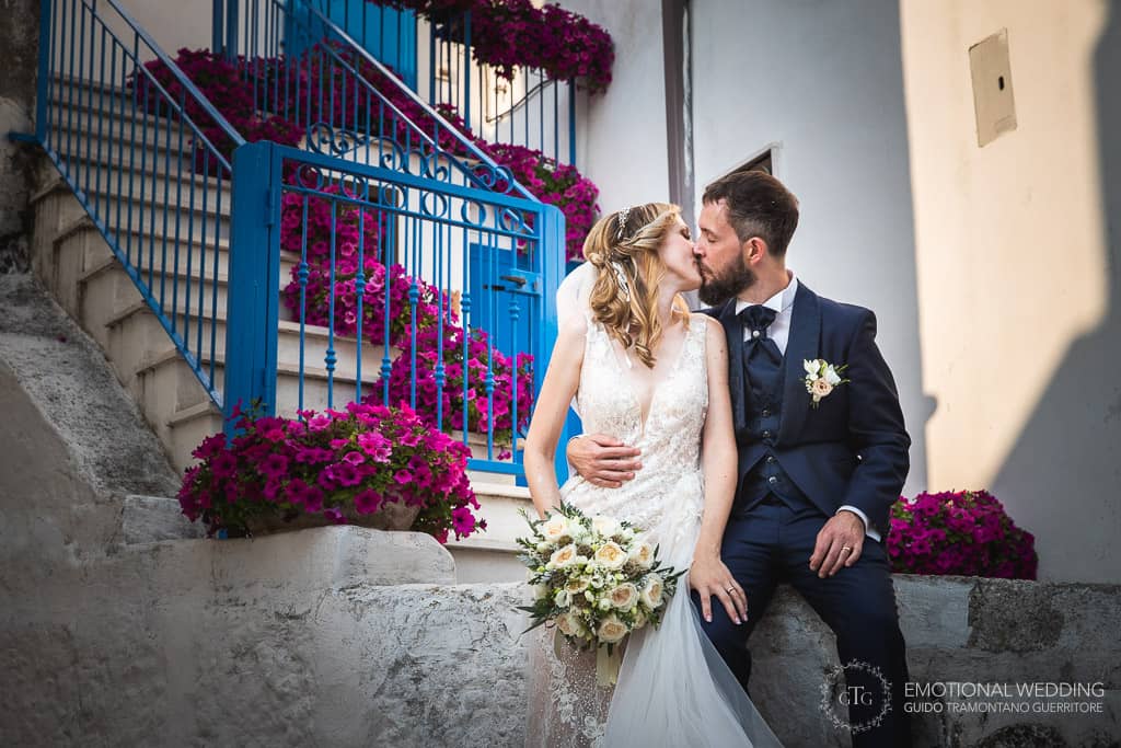 bacio degli sposi seduti sulle scale ornate da fiori a un matrimonio in puglia