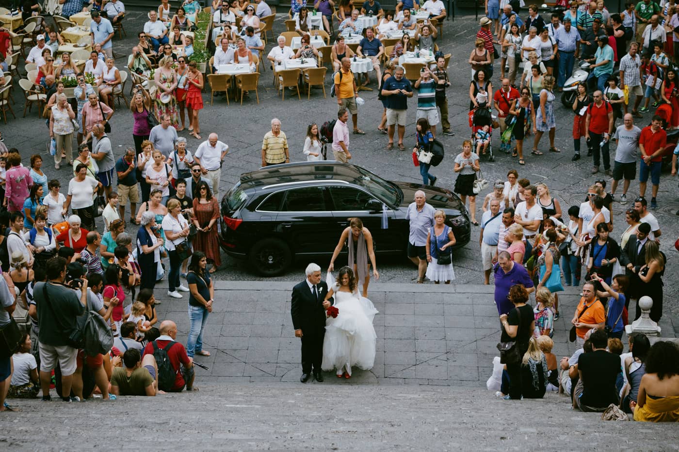 Bride and father climbing the Amalfi Cathedral staircase surrounded by crowd.