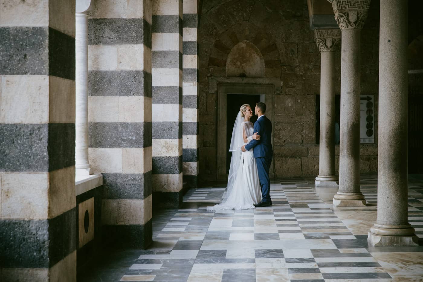 Wedding couple standing by the Arab-Norman striped marble facade of the Amalfi Cathedral.