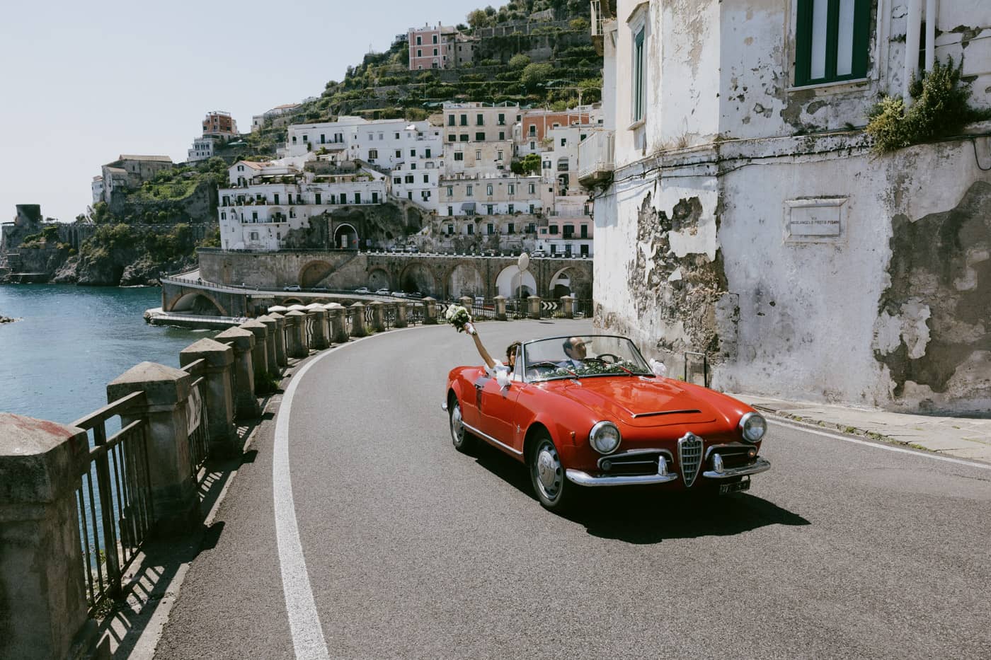Bride and groom driving a vintage red car on the Amalfi Coast.