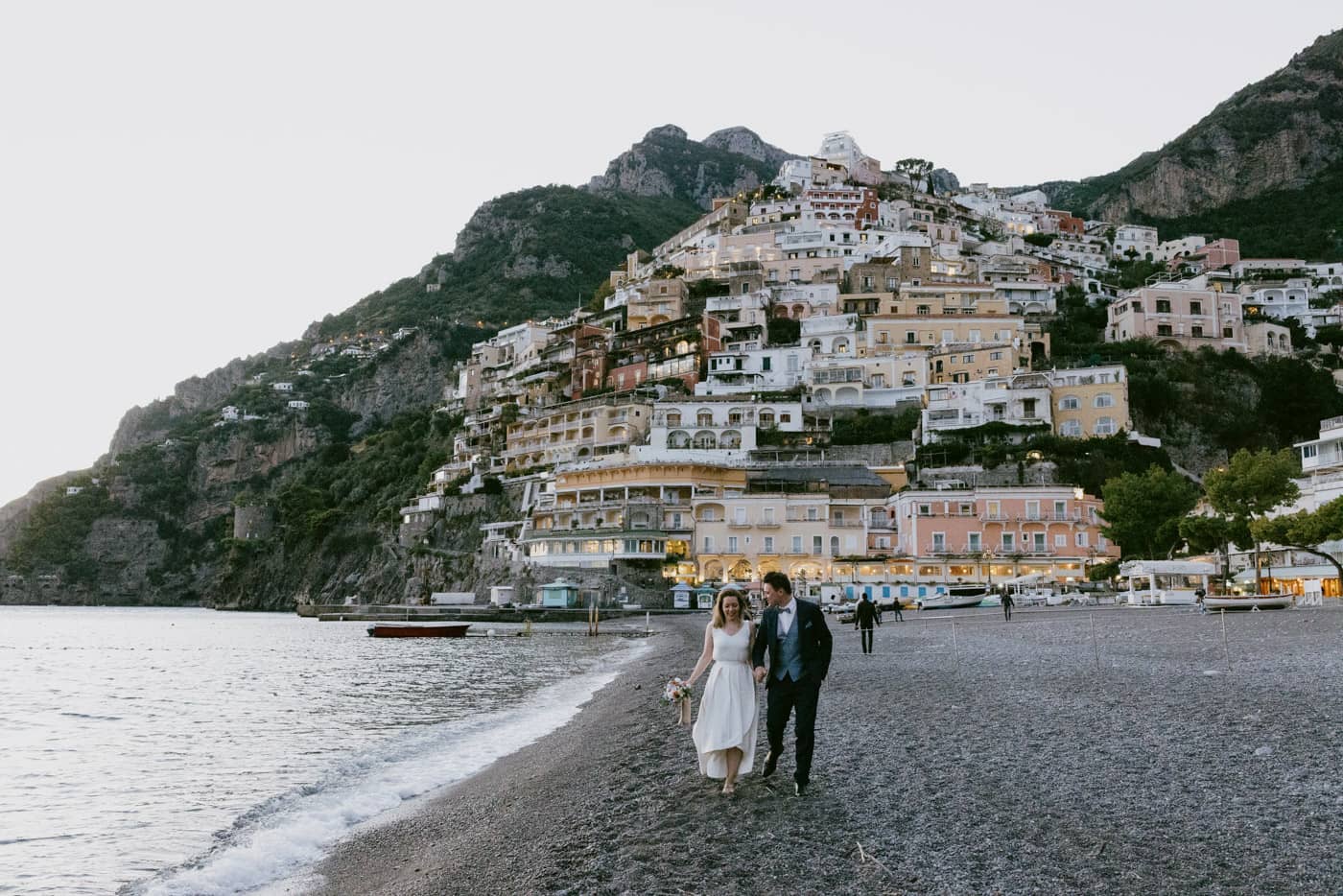 Elopement couple walking hand-in-hand by the water at Spiaggia Grande — Candid photography in Positano, Amalfi Coast.