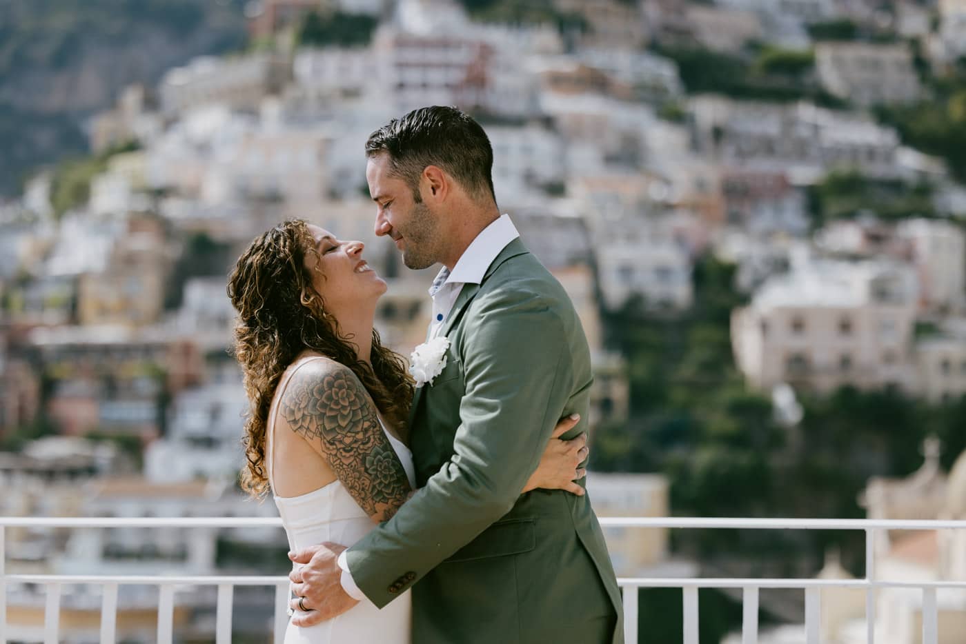 Romantic elopement couple embracing with the iconic Positano village blurred in the background — Positano elopement photographer.