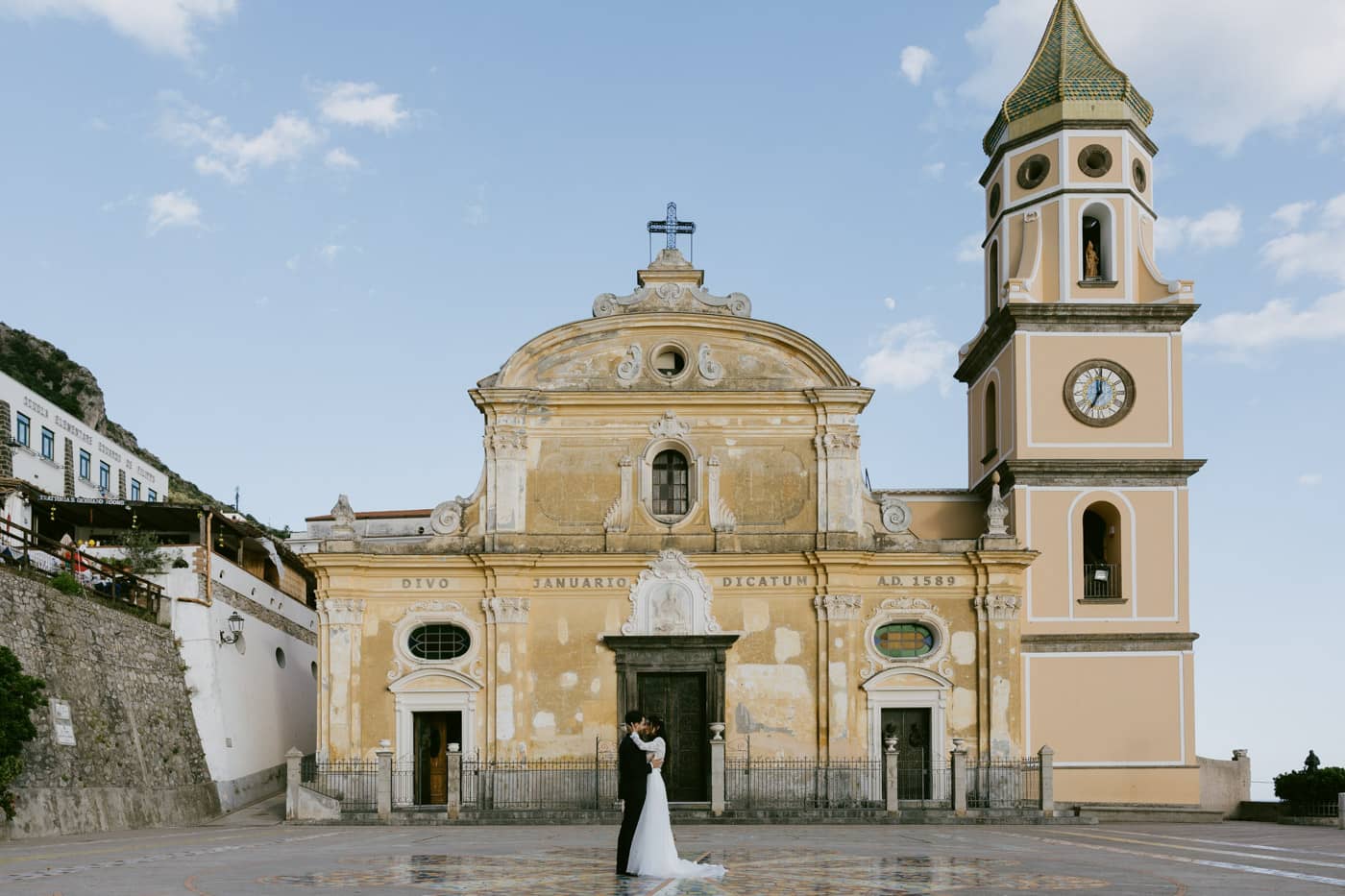 Wedding couple embracing intimately in the sunlit square outside San Gennaro Church — Praiano wedding photographer.