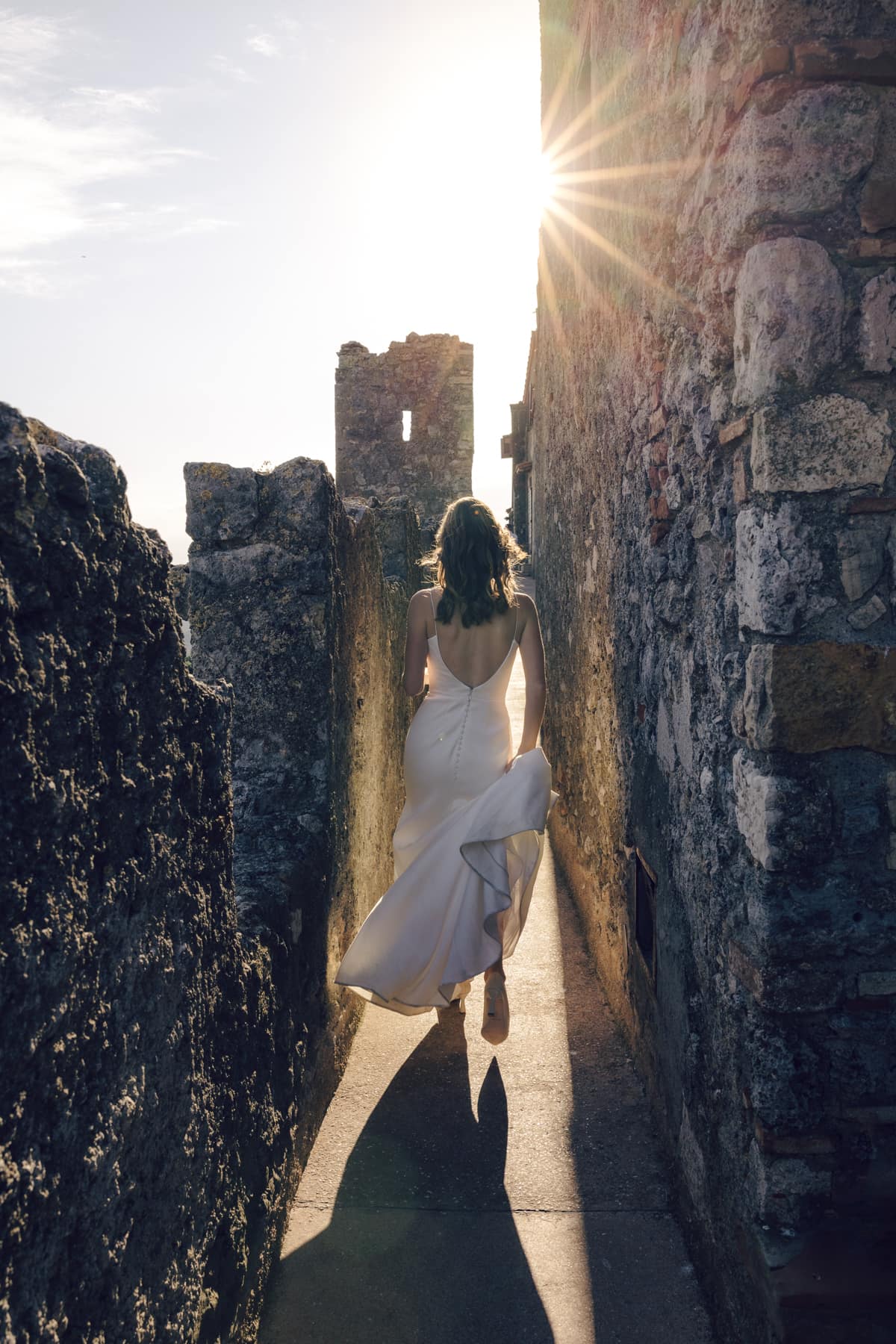 bride in backlight walking among the ancient walls of capalbio in tuscany