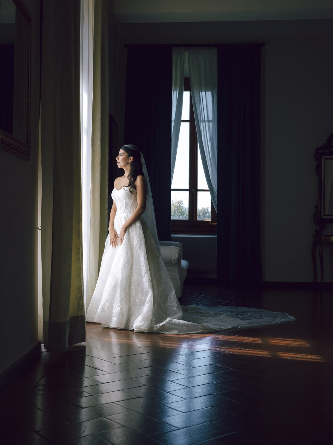 Bride framed inside a grand villa hall looking out through the window in Puglia.