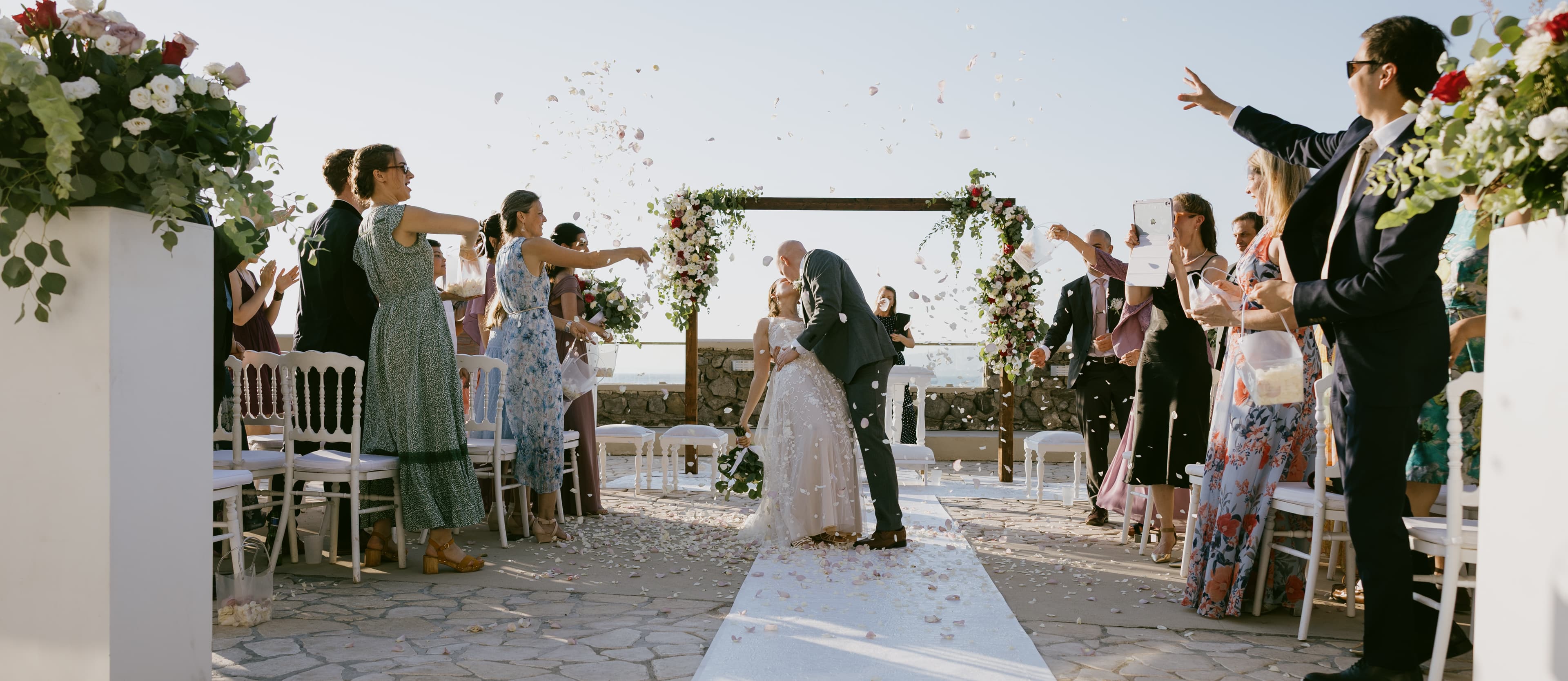 Couple kissing as guests toss flowers after a Sorrento beach ceremony — intimate elopement photography.